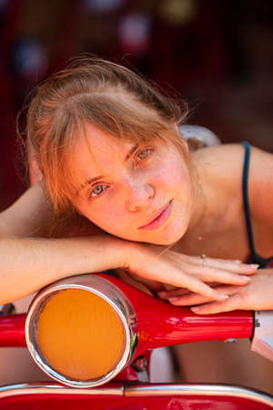 Portrait of young woman posing on a vintage scooter outdoor. Romantic girl with beauty face.の写真素材