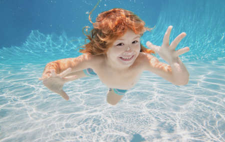 Child underwater. Funny face portrait of child boy swimming and diving underwater with fun in pool.の写真素材