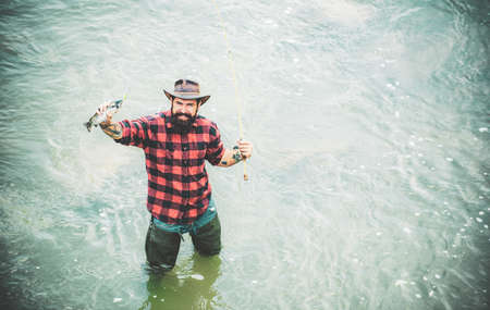 Fisher have fish and long rod. Man relaxing and fishing on river. Happy bearded fisher in water. Having a good time. Active sunny day. Hobby and sport activity. Male hobby.の写真素材
