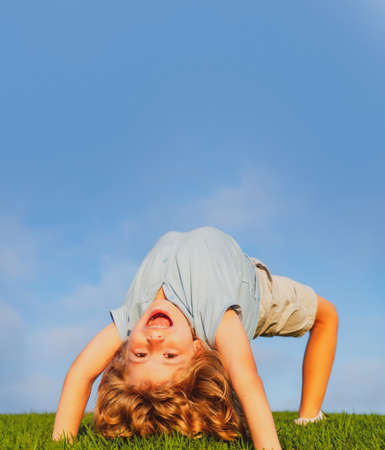 Happy child standing upside down on green grass. Laughing kid boy having fun in spring park. Healthy...