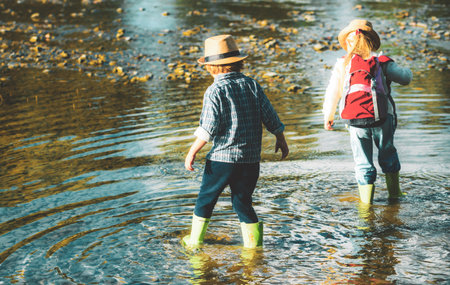 Two kids hiking with backpacks on river. Cute blond girl and boy playing in the creek. Children walking in forest stream and exploring nature. Summer children fun. Children summer activities.の写真素材