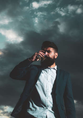 Man with beard and mustache holds alcoholic beverage on sky background. Service and alcoholism concept.の写真素材