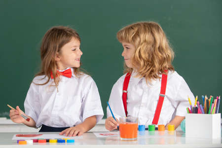 Funny pupils draws in classroom on school blackboard background. School friends kids boy and girl painting together in class. Best children friends enjoying friendship.の写真素材
