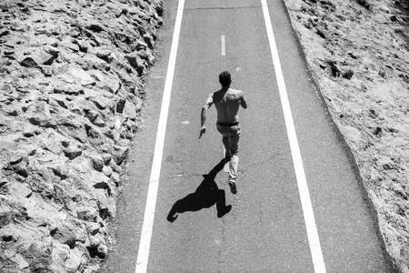 Back view of athletic young man running with naked torso. Sport and fitness runner man running on road training for marathon runの写真素材
