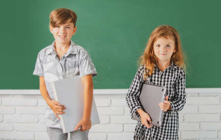 Smiling children hold book with surprising expression against blackboard. School kids friends.の写真素材