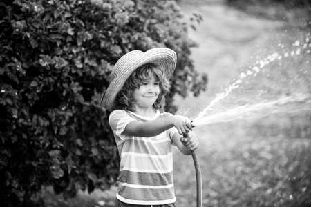 Cute Kid in straw hat is laughing with water spraying hoseの写真素材