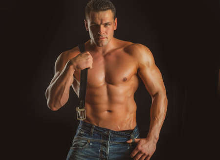 Brutal man with muscular body. Sexy young male holding leather belt. Bad guy.の写真素材