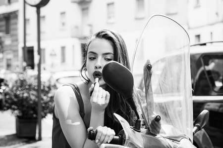 Street makeup. Sexy fashion girl with red lips put lipstick looking in a mirror of motorcycle.の写真素材