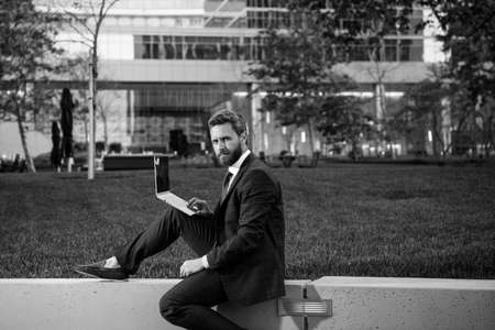 Businessman on large grass field near modern office building. Businessman with laptop in park of megapolice.の写真素材