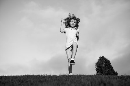 Little boy running and jumping on the grass near a spring green meadow on blue sky. Happy child girl playing on sunny field, summer nature outdoor lifestyle.の写真素材
