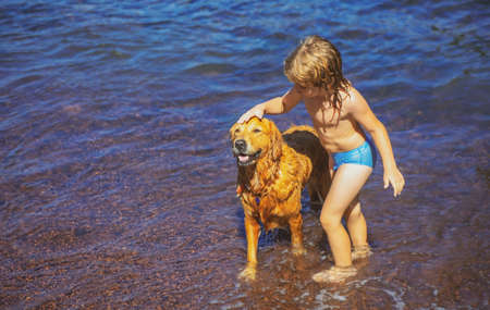 Kid playing with dog on beach. Little boy playing with dog in water.の写真素材