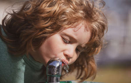 Kids drinking water outdoor in park portrait, close up head of cute child in summer nature park. Thirsty kids.の写真素材