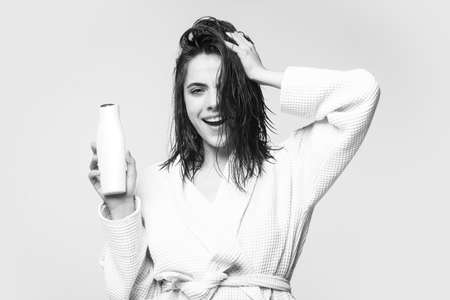 Health hair and beauty concept. A beautiful young girl in the studio with wet hair with balm bottle. Beauty haircare cosmetics. Woman hold bottle shampoo and conditioner.の写真素材