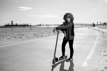 Child on scooter in park. Super hero child in a red superhero coat. Super hero concept.の写真素材
