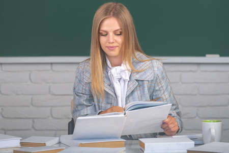Student preparing exam and learning lessons in school classroom. Female student reading book on blackboard background with copy space.の写真素材