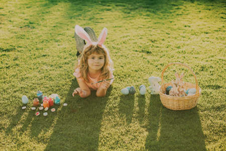 Easter kids boy in bunny ears hunting easter eggs outdoor. Cute child in rabbit costume with bunny ears having fun in park. Easter kids with bunny ears and on grass background.の写真素材
