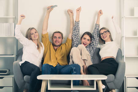 Group of young people sitting on sofa at home. Concept about friendship. Happy excited group watching television and supporting their team with success celebrating victory. Students party.の写真素材