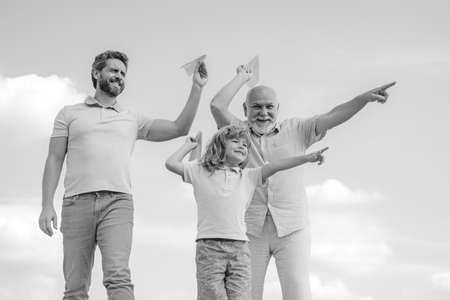 Grandfather father and son playing with paper plane outdoors on sky. Happy family. Three men...