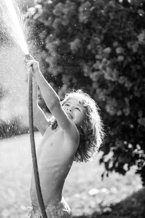 Child watering flowers and plants in garden. Kid with water hose in backyard. Kids gardening. Kids summer fun outdoor at home.の写真素材