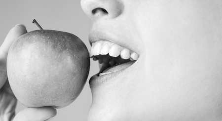 Beautiful young woman eating a apple. Healthy white teeth close up with an apple.の写真素材