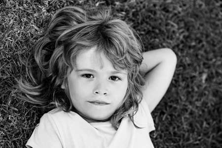 Cute boy lying in the grass. Handsome child enjoying on field or lawn and dreaming.