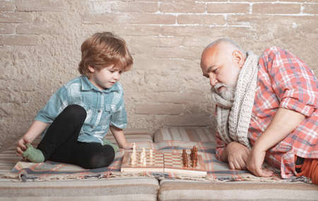 Little boy playing chess with his Grandfather. Chess piece. Senior man thinking about his next move...