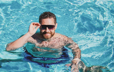 Summer weekend. Handsome man in swimming pool water. Pool spa resort. Summertime vacation.の写真素材
