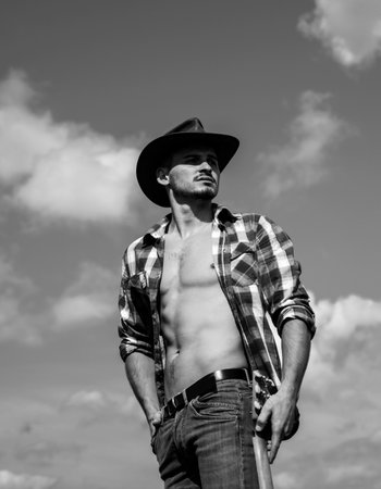 Cowboy couture. Portrait of young man wearing cowboy hat and looking up while standing against sky background. Fashion young man. Handsome guy with confident face.の写真素材