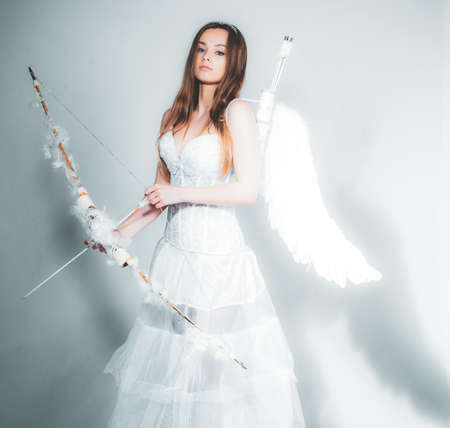 Lovely girl cupid with bow and arrow is ready to find your love. Happy teenage angel girl. Pretty white little girl as the cupid with a bow and arrow congratulating on St Valentines day.の写真素材