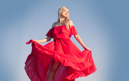Woman in red dress movement on sky. Fashionable young model in style dress. Fashion woman in summer.の写真素材