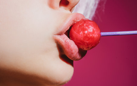 Sensual red lips with candy for print. Red lollipop in the mouth in art design. Glossy womans lips licking sucking lollipop. Sensual sexy mouth with candy concept enjoyment beautiful female lips.の写真素材