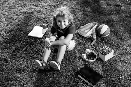 Kid sitting on grass with tablet in the park. Outdoor school.