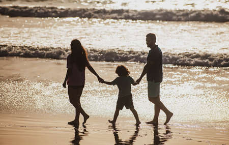 Silhouette of father, mother and child son holding hands and walking on beach.の写真素材