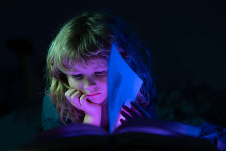 Child reading a book in bed before going to sleep. Little boy lying on bed reading book at home. Happy childhood, dreaming child.の写真素材