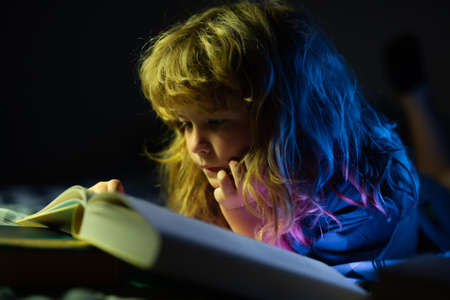A little cute boy reading a book lying on the bed. Development of the child. Clever child boy.の写真素材
