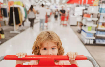 Closeup portrait of kid at grocery or supermarket with goods in shopping trolley.