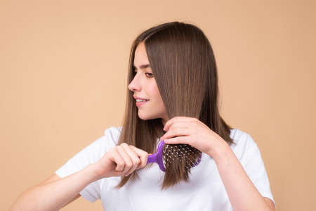 Portrait of charming brunette hair lady combing hair with hairbrush comb, isolated. Young beautiful...