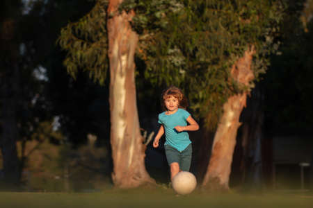 Soccer kids, child boy play football outdoor. Young boy with soccer ball doing kick. Football soccer players in motion. Cute boy in sport action. Child playing football on the playground in park.の写真素材