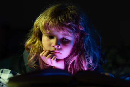 A little cute boy reading a book lying on the bed. Bedtime stories fairy story before bed.の写真素材