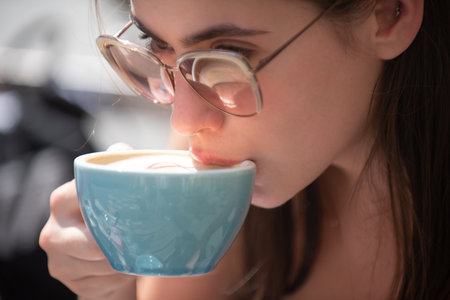 Close up portrait of woman with cup coffee. Girl holding near her lips a cup of hot coffee. Close up woman lip with mouth drink latte.の写真素材