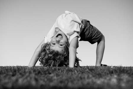 Child boy upside down outdoors in sunny summer day. Happy child laying on green grass. Funny kid outdoor in spring garden. Earth day and healthy lifestyle concept.の写真素材