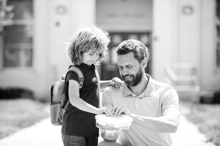 School lunch for kids. Father supports and motivates son. Schoolboy and parent in shirt holding lunch box.の写真素材