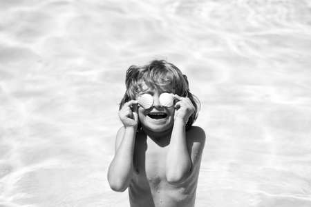 Little boy playing in outdoor swimming pool in blue water on summer vacation on tropical beach. Child learning to swim in pool of luxury resort.の写真素材