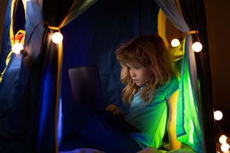 Little kid using laptop by night, child boy illuminated by the blue light of a computer screen.の写真素材