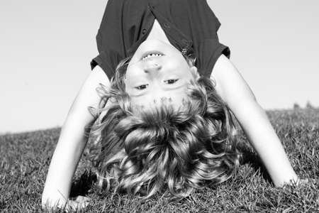 Portrait of a happy smiling child boy playing upside down on grass field outdoor. Laughing child....