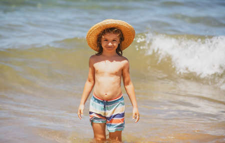 Adorable little boy in straw hat at beach during summer vacation. Portrait of playful kid on the sea background. Funny summer child face.の写真素材