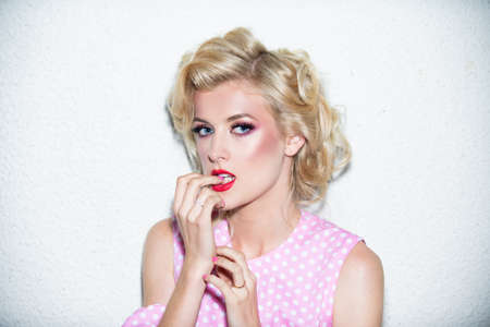 Sensual blonde female model with red lips and bright make up bite nails. Young beautiful sexy woman face with beauty make-up.の写真素材
