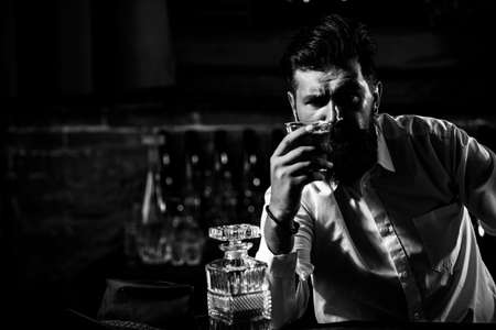 Young man holding glass of whiskey. Guy with beard holds brandy. Bearded drink cognac. Sommelier tastes drink. Man holding a glass of whisky. Sipping whiskey. Degustation, tastingの写真素材