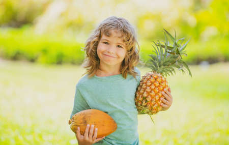Child boy holding pineapple and coconut smiling with happy face. Summer fruits.の写真素材