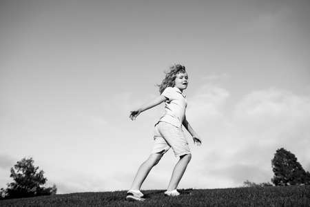 Kid running on grass field. Cute boy run in summer park. Child running on meadow.の写真素材